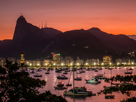 View of Botafogo Bay with sailboats city skyline and silhouette of Corcovado Mountain under a vibrant sunset sky Rio de Janeiro State of Rio de Janeiro Brazil.