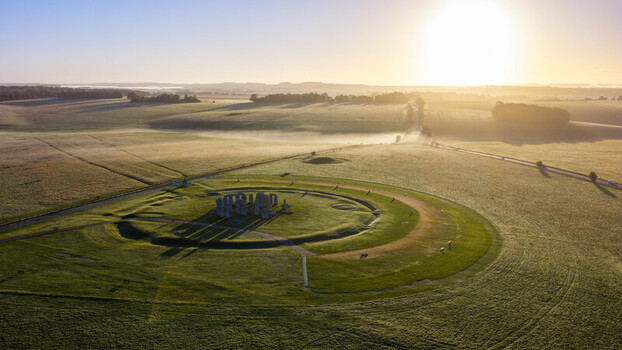 Aerial view of Stonehenge surrounded by lush green fields and morning mist at sunrise in Salisbury England United Kingdom. Aerial view of Stonehenge surrounded by lush green fields and morning mist at sunrise in Salisbury England United Kingdom.