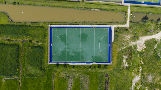 Aerial view of H.C. Rijnvliet hockey pitch featuring green artificial turf and an adjacent canal surrounded by lush fields in Utrecht Utrecht Netherlands.
