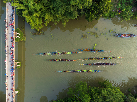 Aerial view of the vibrant boat race cutting through the murky river while spectators throng the bridge Gopalganj Dhaka Division Bangladesh. Aerial view of the vibrant boat race cutting through the murky river while spectators throng the bridge Gopalganj Dhaka Division Bangladesh.