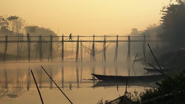 View of people on a bamboo bridge over a river at sunrise Bangladesh.