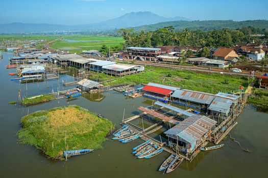 Aerial view of Spot Mancing Sumurup Rawapening with floating fishing huts small blue boats and a railway track near the lake in Semarang Regency Central Java Indonesia.