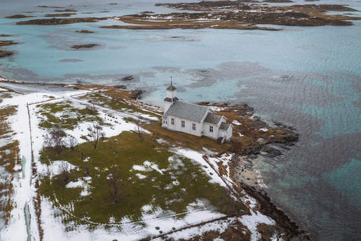 Aerial view of a quaint white church standing sentinel against the icy turquoise waters and snow dusted shores Gimsøysand Nordland Norway. Aerial view of a quaint white church standing sentinel against the icy turquoise waters and snow dusted shores Gimsøysand Nordland Norway.