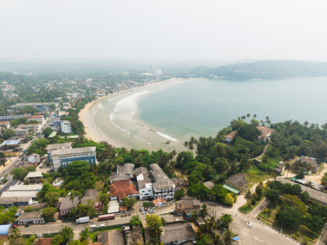 Aerial view of Dewata Beach Road and the curved coastline of Galle Bay with its sandy shore turquoise waves and lush tropical greenery in Galle Southern Province Sri Lanka.