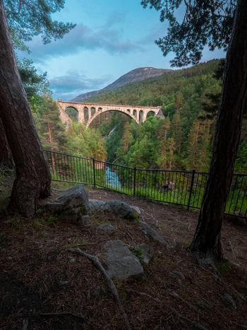 View of the historic stone arch Kylling Bridge spanning a deep river valley surrounded by dense pine forests and mountains in Rauma Municipality More og Romsdal Norway. View of the historic stone arch Kylling Bridge spanning a deep river valley surrounded by dense pine forests and mountains in Rauma Municipality More og Romsdal Norway.