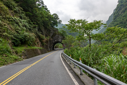 View of a mountain road passing through a tunnel in Taroko National Park surrounded by lush green cliffs and dense vegetation in Xiulin Township Hualien County Taiwan.