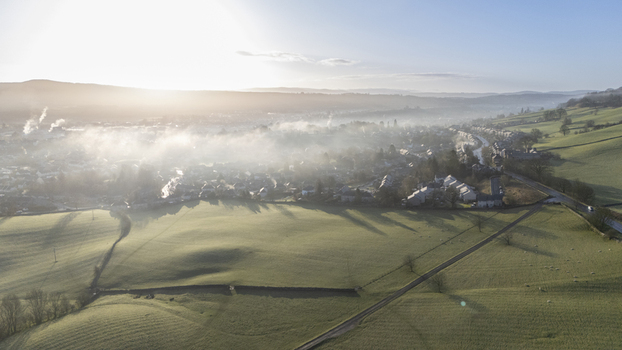 Aerial view of the village nestled in the embrace of morning mist with fields painted in contrasting shades of green and gold Bakewell England United Kingdom. Aerial view of the village nestled in the embrace of morning mist with fields painted in contrasting shades of green and gold Bakewell England United Kingdom.