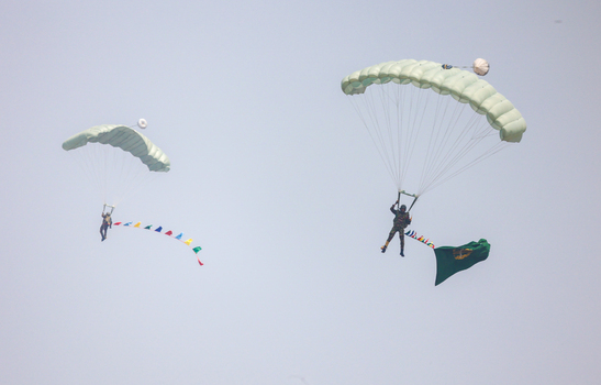 Dhaka Bangladesh 25 March 2026 View of skydivers gracefully descending through the vast open sky one trailing a vibrant banner of colorful flags another bearing the national flag.