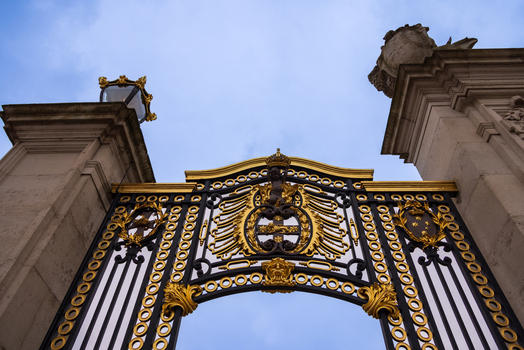 London United Kingdom 12 May 2025 View of the ornate gold and black wrought iron gates of Buckingham Palace against a blue sky.