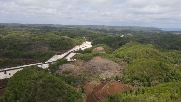 Aerial view of a new road under construction winding through lush green hills and terraced fields in Tanjungsari Special Region of Yogyakarta Indonesia. Aerial view of a new road under construction winding through lush green hills and terraced fields in Tanjungsari Special Region of Yogyakarta Indonesia.