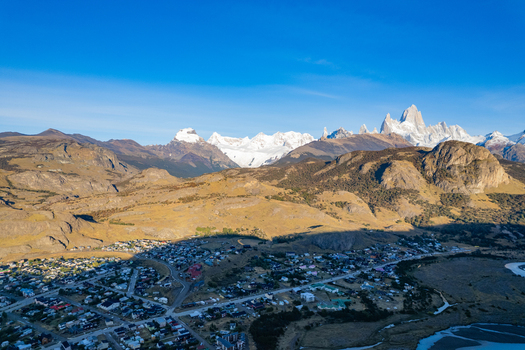 Aerial view of the town of El Chalten nestled in the Patagonian landscape with the iconic Mount Fitz Roy in the background golden hills and clear blue sky El Chalten Santa Cruz Argentina. Aerial view of the town of El Chalten nestled in the Patagonian landscape with the iconic Mount Fitz Roy in the background golden hills and clear blue sky El Chalten Santa Cruz Argentina.