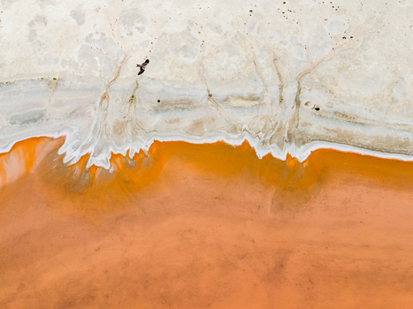 Aerial view of a salt lake in the Mallee region featuring vibrant orange water white salt crust patterns and a bird flying over the landscape in Woorinen North Victoria Australia. Aerial view of a salt lake in the Mallee region featuring vibrant orange water white salt crust patterns and a bird flying over the landscape in Woorinen North Victoria Australia.