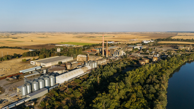Aerial view of an industrial facility with grain silos and tall chimneys situated along the Sava River surrounded by vast agricultural fields in Sremska Mitrovica Vojvodina Serbia. Aerial view of an industrial facility with grain silos and tall chimneys situated along the Sava River surrounded by vast agricultural fields in Sremska Mitrovica Vojvodina Serbia.
