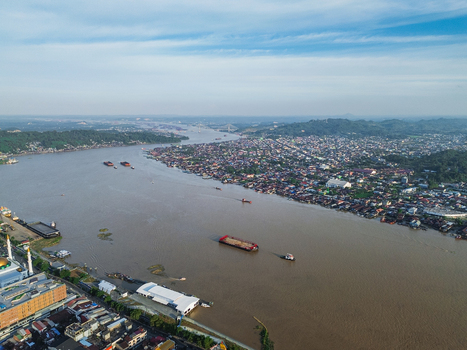 Aerial view of the Mahakam River flowing through the city with coal barges dense urban housing and a mosque along the riverbank in Samarinda Kalimantan Timur Indonesia. Aerial view of the Mahakam River flowing through the city with coal barges dense urban housing and a mosque along the riverbank in Samarinda Kalimantan Timur Indonesia.