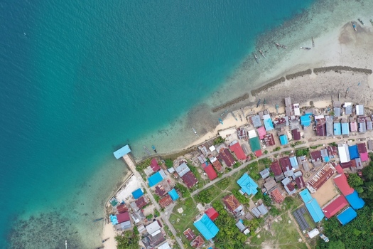 Aerial view of Pulau Maginti featuring a coastal village with colorful houses a wooden pier and small boats moored along the turquoise shoreline Maginti South East Sulawesi Indonesia.