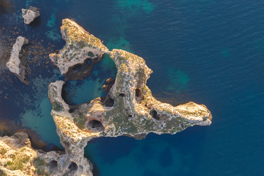 Aerial view of the dramatic limestone rock formations and sea arches of Ponta da Piedade surrounded by turquoise and deep blue Atlantic Ocean waters in Lagos Faro District Portugal.