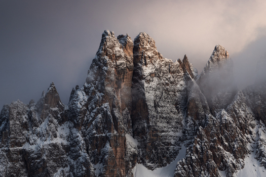 View of the jagged snow covered peaks of the Dolomites partially shrouded in mist and clouds under a soft light Trentino Alto Adige Italy. View of the jagged snow covered peaks of the Dolomites partially shrouded in mist and clouds under a soft light Trentino Alto Adige Italy.