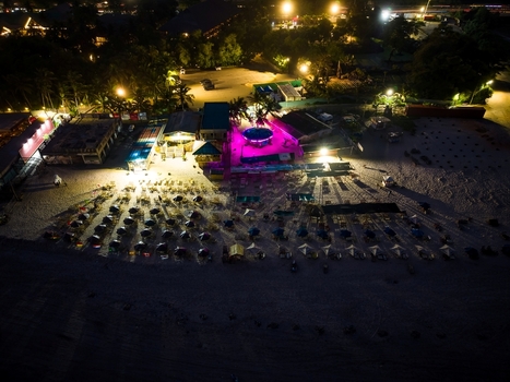 Aerial view of a beach resort at night with illuminated structures rows of umbrellas on the sand and vibrant purple lighting in Ghana.