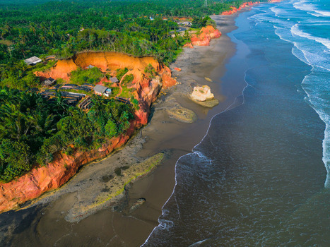 Aerial view of the dramatic red clay cliffs meeting the dark sand beach and turquoise ocean waves in Bali Bali Indonesia. Aerial view of the dramatic red clay cliffs meeting the dark sand beach and turquoise ocean waves in Bali Bali Indonesia.