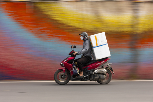 Hanoi Ha Noi Vietnam 11 November 2025 View of a delivery driver riding a red scooter with a large white box on the back passing a colorful mural in the city.