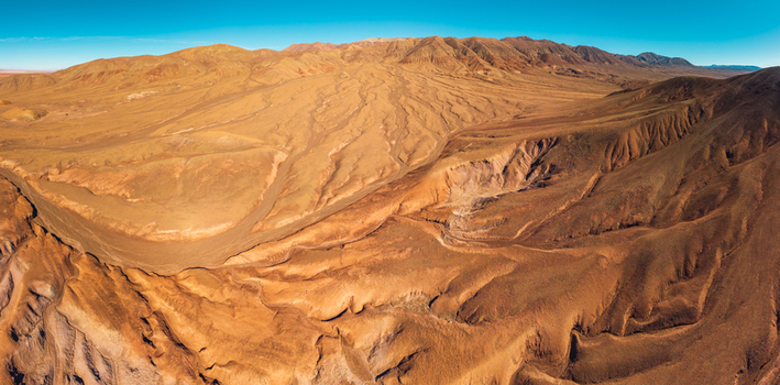 Aerial view of the arid rugged desert landscape with deep erosion gullies rolling hills and vast sandy terrain under a clear blue sky in San Pedro de Atacama Antofagasta Chile. Aerial view of the arid rugged desert landscape with deep erosion gullies rolling hills and vast sandy terrain under a clear blue sky in San Pedro de Atacama Antofagasta Chile.