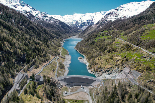 Aerial view of the Beauregard Dam and the turquoise waters of Lake Beauregard surrounded by snow capped Alpine peaks and green mountain slopes in Valgrisenche Aosta Valley Italy.