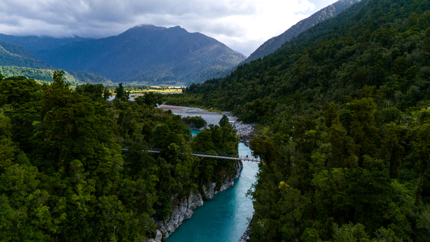 Aerial view of the Hokitika Gorge s turquoise waters snaking between lush green forests and rocky cliffs a suspension bridge adding a human touch to the wild landscape Hokitika Gorge New Zealand. Aerial view of the Hokitika Gorge s turquoise waters snaking between lush green forests and rocky cliffs a suspension bridge adding a human touch to the wild landscape Hokitika Gorge New Zealand.