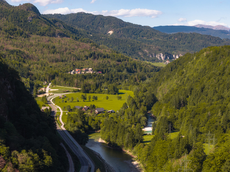 Aerial view of the Sava Bohinjka river winding through a lush green valley with forested hills a winding road and small houses in Radovljica Slovenia.