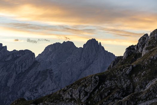 View of rugged mountain peaks pierce the soft glow of the sunset sky casting long shadows across the rocky terrain Picos de Europa Asturias Spain.