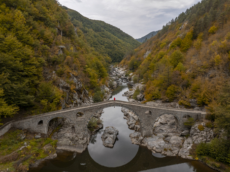 Aerial view of Devil s Bridge spanning the Arda River in a lush valley with autumn foliage and rocky terrain in Kardzhali Province Bulgaria. Aerial view of Devil s Bridge spanning the Arda River in a lush valley with autumn foliage and rocky terrain in Kardzhali Province Bulgaria.