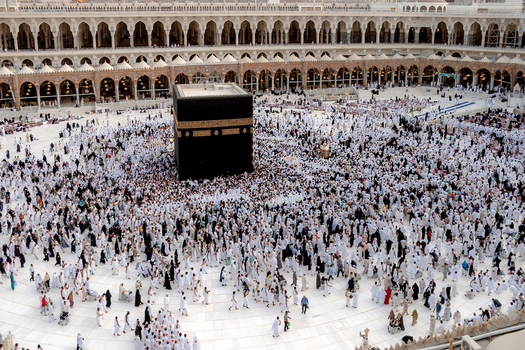 Aerial view of the Kaaba at Masjid al Haram surrounded by pilgrims in white garments with historic arched colonnades in Makkah Makkah Province Saudi Arabia. Aerial view of the Kaaba at Masjid al Haram surrounded by pilgrims in white garments with historic arched colonnades in Makkah Makkah Province Saudi Arabia.