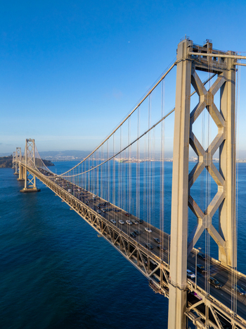 Aerial view of the San Francisco Oakland Bay Bridge with traffic flowing across the suspension structure over the blue waters of the bay in San Francisco California United States. Aerial view of the San Francisco Oakland Bay Bridge with traffic flowing across the suspension structure over the blue waters of the bay in San Francisco California United States.