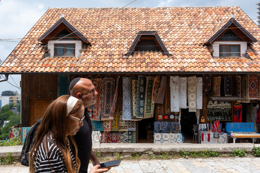Kruje Albania 12 June 2026 View of a traditional shop in the Old Bazaar with colorful handmade rugs hanging on wooden walls under a tiled roof as people walk by.