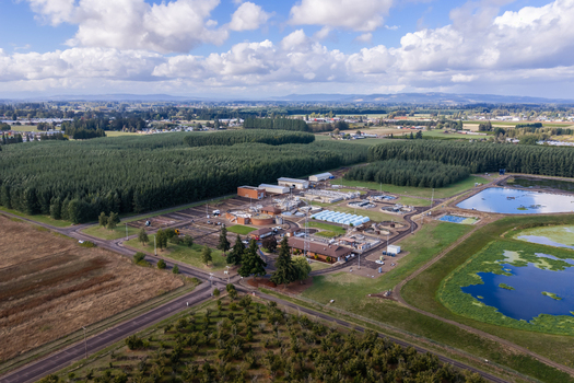 Aerial view of the wastewater treatment plant surrounded by agricultural fields lush green trees and settling ponds under a blue sky with white clouds in Woodburn Oregon United States. Aerial view of the wastewater treatment plant surrounded by agricultural fields lush green trees and settling ponds under a blue sky with white clouds in Woodburn Oregon United States.