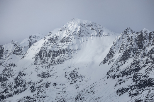 View of snow covered mountain peaks and rugged rocky slopes under an overcast sky in Ersfjord Troms Norway. View of snow covered mountain peaks and rugged rocky slopes under an overcast sky in Ersfjord Troms Norway.