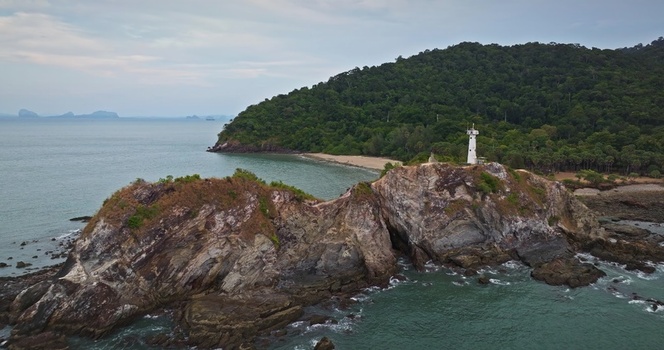 Aerial view of a lighthouse perched on a rocky headland surrounded by lush green forest and the ocean along the coastline of Thailand. Aerial view of a lighthouse perched on a rocky headland surrounded by lush green forest and the ocean along the coastline of Thailand.