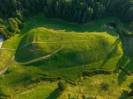 Aerial view of the Seimyniskeliai Mound Historical Complex a grassy hillfort surrounded by lush forest and green meadows with a wooden walkway in Anyksciai Utena County Lithuania.