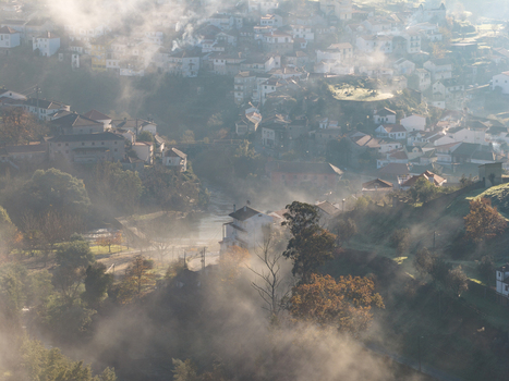 Aerial view of the historic village of Avo shrouded in morning mist with white houses and orange rooftops nestled in a lush valley Oliveira do Hospital Coimbra District Portugal.