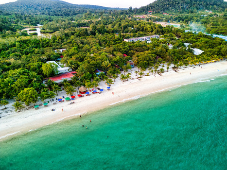 Aerial view of the pristine white sands meeting the turquoise waters fringed by lush green trees and colorful umbrellas Preah Sihanouk Sihanoukville Cambodia.
