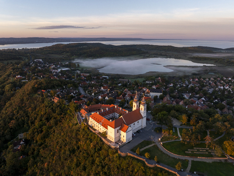 Aerial view of Tihany Abbey surrounded by historic buildings lush green hills and the misty waters of Lake Balaton at sunset in Tihany Hungary. Aerial view of Tihany Abbey surrounded by historic buildings lush green hills and the misty waters of Lake Balaton at sunset in Tihany Hungary.