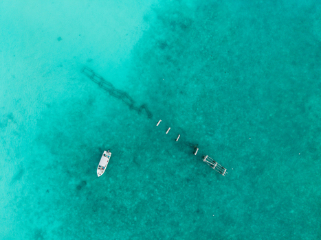 Aerial view of a white boat on vivid turquoise water with a dark underwater structure Hoarafushi Thiladhunmathee Uthuruburi Maldives. Aerial view of a white boat on vivid turquoise water with a dark underwater structure Hoarafushi Thiladhunmathee Uthuruburi Maldives.