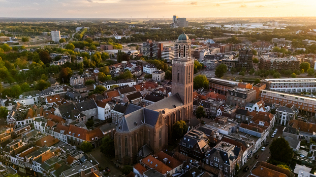 Aerial view of the historic Grote Kerk surrounded by dense urban rooftops and winding streets during the golden hour in Zwolle Overijssel Netherlands.