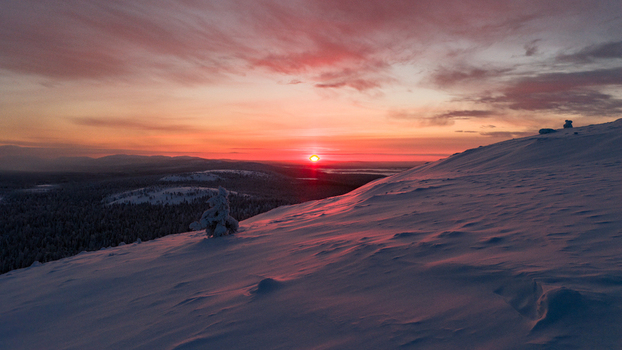 Aerial view of the snow covered fells of Luosto under a vibrant red sunset sky with frozen forests in Sodankyla Lapland Finland. Aerial view of the snow covered fells of Luosto under a vibrant red sunset sky with frozen forests in Sodankyla Lapland Finland.