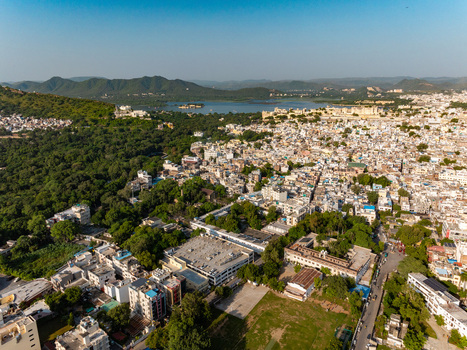 Aerial view of the historic city of Udaipur with its dense urban rooftops lush green hills and the expansive Lake Pichola in the background Udaipur Rajasthan India.