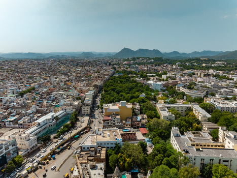 Aerial view of the city of Udaipur with its dense urban landscape historic buildings lush green trees and distant mountains in Udaipur Rajasthan India.