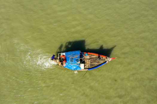 Aerial view of a traditional wooden fishing boat with a blue tarp cover moving through calm waters near the coast of Kuakata Barisal Division Bangladesh. Aerial view of a traditional wooden fishing boat with a blue tarp cover moving through calm waters near the coast of Kuakata Barisal Division Bangladesh.