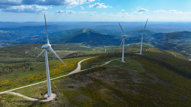 Aerial view of wind turbines situated on rolling hills covered with yellow wildflowers and green vegetation under a bright blue sky in Lisbon Lisbon Portugal. Aerial view of wind turbines situated on rolling hills covered with yellow wildflowers and green vegetation under a bright blue sky in Lisbon Lisbon Portugal.