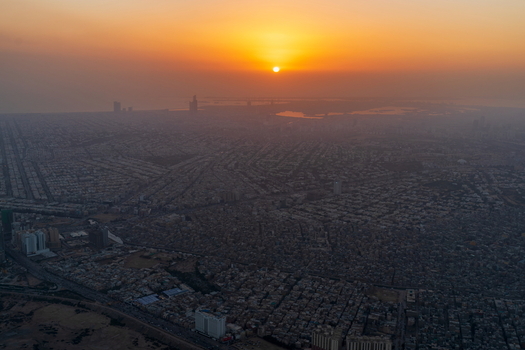Aerial view of the sprawling cityscape of Karachi at sunset with golden light illuminating the dense urban grid and distant coastline. Karachi Sindh Pakistan.