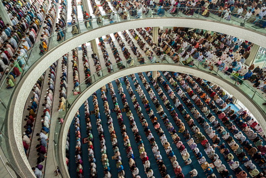 Dhaka Bangladesh 19 June 2026 Aerial view of a large congregation of worshippers praying inside a modern mosque with rows of people kneeling on blue carpets.