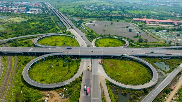 Aerial view of the JNPT Interchange featuring multi level highway ramps surrounding greenery and vehicles on the road in Navi Mumbai Maharashtra India.